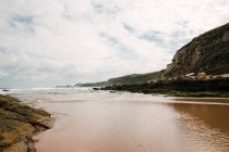 Живописный вид на зеленую гору на песчаном берегу против пенного океана с горизонтом в Кантабрии Испания — стоковое фото