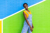Side view of happy young African American female smiling while standing on colorful bright wall — Stock Photo