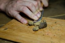 Cultivar macho irreconhecível com faca trituração peça planta de cannabis seca em tábua de madeira no espaço de trabalho — Fotografia de Stock