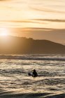Rückenansicht einer jungen Frau mit Surfbrett im Meer bei Sonnenuntergang am Strand in Asturien, Spanien — Stockfoto