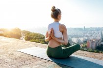 Сверху сзади вид анонимной гибкой женщины с молящимися руками за спиной практикующей йогу на коврике в солнечном городе — стоковое фото