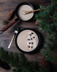 De cima de tigelas pretas com sopa de creme de castanhas colocadas em mesa de madeira com ramos verdes de abeto com cones — Fotografia de Stock