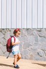 Seitenansicht eines Schulkindes mit Rucksack auf dem Bürgersteig, das sich im Sonnenlicht freut — Stockfoto