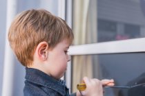 Seitenansicht des fokussierten Kindes, das lernt, wie man Schraubenzieher bedient, während es tagsüber im Fenster reflektiert — Stockfoto