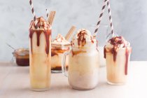 Асорті окуляри з солодким карамельним молочним коктейлем з ванільним морозивом та вафельним печивом, поданим на столі — стокове фото