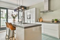 Elegante interno di cucina moderna con armadi bianchi ed elettrodomestici e lavandino nel bancone sopra il bancone in grande casa con parete di vetro — Foto stock