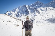 Rückansicht eines nicht wiederzuerkennenden Forschers mit Rucksack, der auf einem felsigen Steilhang des schneebedeckten Berges steht, während er im Hochland Nepals unterwegs ist — Stockfoto