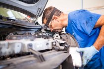 Side view of busy mature male technician fixing engine of broken car in spacious facility of repair service — Stock Photo