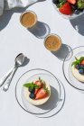 Bolos de queijo saborosos com morangos frescos e mirtilos sob folhas de hortelã contra tiros de café expresso na mesa na cafetaria — Fotografia de Stock