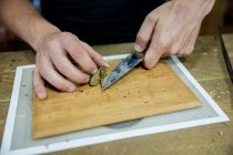 Crop unrecognizable male with knife cutting dried cannabis plant piece on wooden board in workspace — Stock Photo