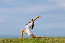 Side view of young ethnic female in sportswear standing in Ashta Chandrasana pose during yoga practice on sea shore — Stock Photo