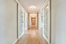 Empty hallway with white walls and parquet floor and doors leading to exit in modern light apartment — Stock Photo