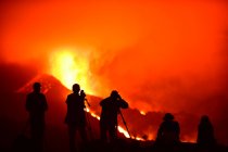 Silhouette umane che registrano e fotografano con treppiedi la lava esplosa nelle Isole Canarie di La Palma 2021 e due silhouette sedute che osservano il fenomeno naturale. — Foto stock