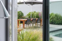 Интерьер комнаты с окном с видом на террасу с зелеными растениями и деревянным столом в дневное время — стоковое фото