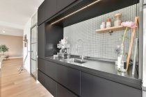 Современная кофеварка размещена на темной кухне возле раковины в современной кухне с черными шкафами в квартире в дневное время — стоковое фото