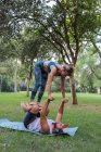 Duración completa de la pareja concentrada en ropa deportiva haciendo asana mientras practican acroyoga juntos en el parque verde a la luz del día - foto de stock