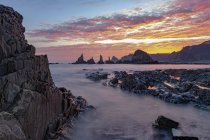 Cenário espetacular com ondas marinhas espumosas lavando formações rochosas ásperas de várias formas na praia selvagem de Geirua, nas Astúrias Espanha, durante o pôr do sol — Fotografia de Stock