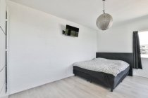 Черная кровать и телевизор в современной спальне с белыми стенами в квартире, оформленной в минимальном стиле — стоковое фото