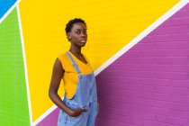 Vista lateral de la joven mujer afroamericana de pie en la pared brillante colorido - foto de stock