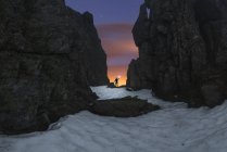 Tourist mit Fackel auf sandigem Land zwischen rauen Bergen unter bewölktem Himmel mit Sternen bei Sonnenuntergang — Stockfoto
