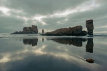 Paesaggio panoramico di riva sabbiosa bagnata con formazioni rocciose sotto il cielo nuvoloso con luce solare in serata sulla spiaggia Playon de Bayas in Asturais Spagna — Foto stock