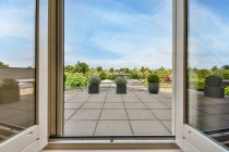 Porta contra plantas em vasos na varanda sob céu azul nublado no dia de verão na luz solar — Fotografia de Stock