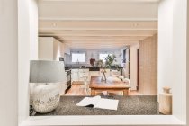 Durch Fenster des zeitgenössischen Interieurs der geräumigen Küche mit Esstisch und verschiedenen Geräten im Ferienhaus — Stockfoto