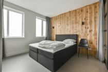 Комфортабельная кровать с белым бельем, прислоненная к деревянной стене в спальне с минималистичным дизайном — стоковое фото
