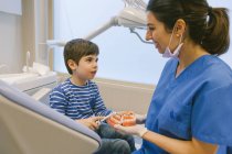 Усміхнена жінка-ортодонта навчає пацієнта зубною щіткою чистити зуби на моделі щелепи в стоматологічній клініці — стокове фото