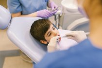 Alto ángulo de cultivo dentista y asistente de tratamiento de dientes de niño durante el procedimiento en la clínica de odontología - foto de stock