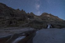 Spettacolare scenario di formazioni rocciose grezze con cascata che scorre verso il lago sotto il cielo stellato senza nuvole di notte — Foto stock