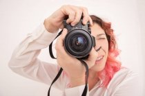 Photographe femelle pensive avec des cheveux roses prenant des photos sur appareil photo professionnel dans la salle de lumière — Photo de stock