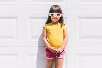 Menina bonito alegre em roupas coloridas casuais e óculos tridimensionais em pé no fundo da parede branca — Fotografia de Stock