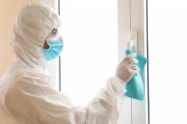 Vista laterale del medico maschile in dispositivi di protezione individuale maniglia di pulizia della finestra con straccio durante la pandemia di COVID 19 in ospedale — Foto stock