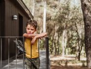 Bambino in piedi sulla veranda del cottage moderno situato nel bosco in estate — Foto stock