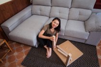 Young attentive ethnic female mounting table on ornamental carpet against sofa in light house room — Stock Photo