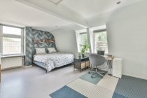 Кровать с белым бельем, расположенная рядом с рабочим местом, с открытым ноутбуком в просторной светлой спальне в квартире — стоковое фото