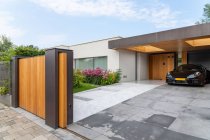 Moderner Sportwagen parkt im Hinterhof einer stilvollen minimalistischen Villa, die an sonnigen Tagen mit blühenden Pflanzen dekoriert ist — Stockfoto