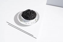Von oben Keramikschale mit leckeren Spaghetti mit schwarzer Tintenfischtinte mit Essstäbchen auf weißem Hintergrund — Stockfoto