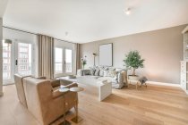Fauteuils et canapé confortables placés dans un salon spacieux avec un intérieur minimaliste dans un appartement de luxe à la lumière du jour — Photo de stock