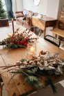 Von oben festlicher Weihnachtsstrauß mit Baumwollzweigen, Tannenzweigen und Eukalyptuszweigen und leuchtend roten Zweigen mit Beeren auf Holztisch mit Kerzen im Zimmer — Stockfoto