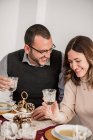 Crop cheerful couple with glasses of alcoholic beverage interacting while laughing at table with cream soups during New Year holiday — Stock Photo