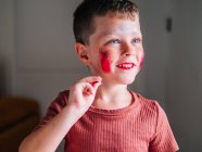 Messy child with brown hair and cosmetic on face in light house on blurred background — Stock Photo