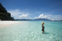 Вид сбоку этнической туристки в купальнике и соломенной шляпе, стоящей в прозрачном море во время поездки в Малайзию — стоковое фото