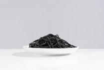 Мінімалістична студія з чорними кальмарами спагетті в повному керамічному посуді на білому столі — стокове фото