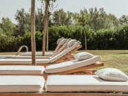 Espreguiçadeiras brancas colocadas em fila perto da piscina no jardim verde do resort no dia ensolarado no verão — Fotografia de Stock