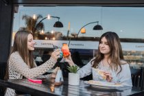 Весела жінка-підліток взаємодіє під час клонування келихів смачних освіжаючих напоїв за столом у міських кафетеріях — стокове фото