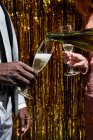 Cultiver femme anonyme verser du champagne de la bouteille dans un verre de petit ami noir pendant la célébration du Nouvel An contre tinsel — Photo de stock