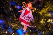 Decoraciones en forma de ángel y estrella colgando de ramas de abeto artificial de Navidad que brillan por la noche - foto de stock