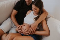Cropped homme embrassant ventre de femme enceinte bien-aimée tout en se reposant sur le canapé dans le salon — Photo de stock